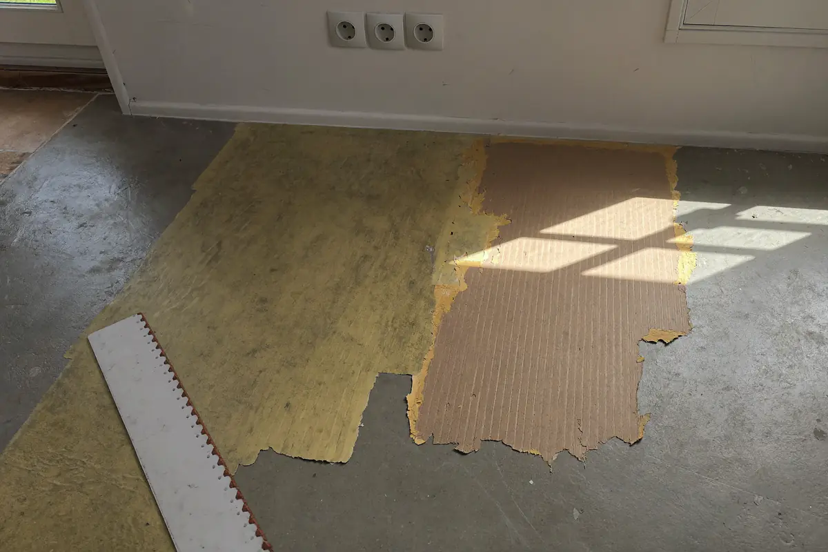 Close-up van een dekvloer vol bruine en gele lijmresten na het verwijderen van een oude vloer